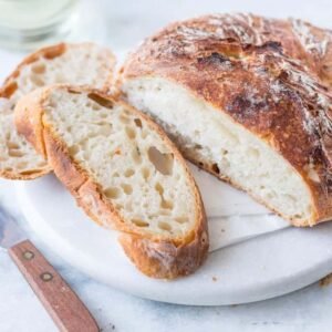 Rustic white bread loaf with visible crumb structure and sliced portions on a white plate.