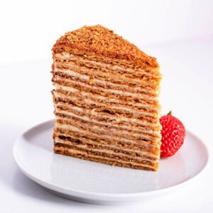 Medovik cake slice with honey layers and crumb topping, alongside a strawberry.